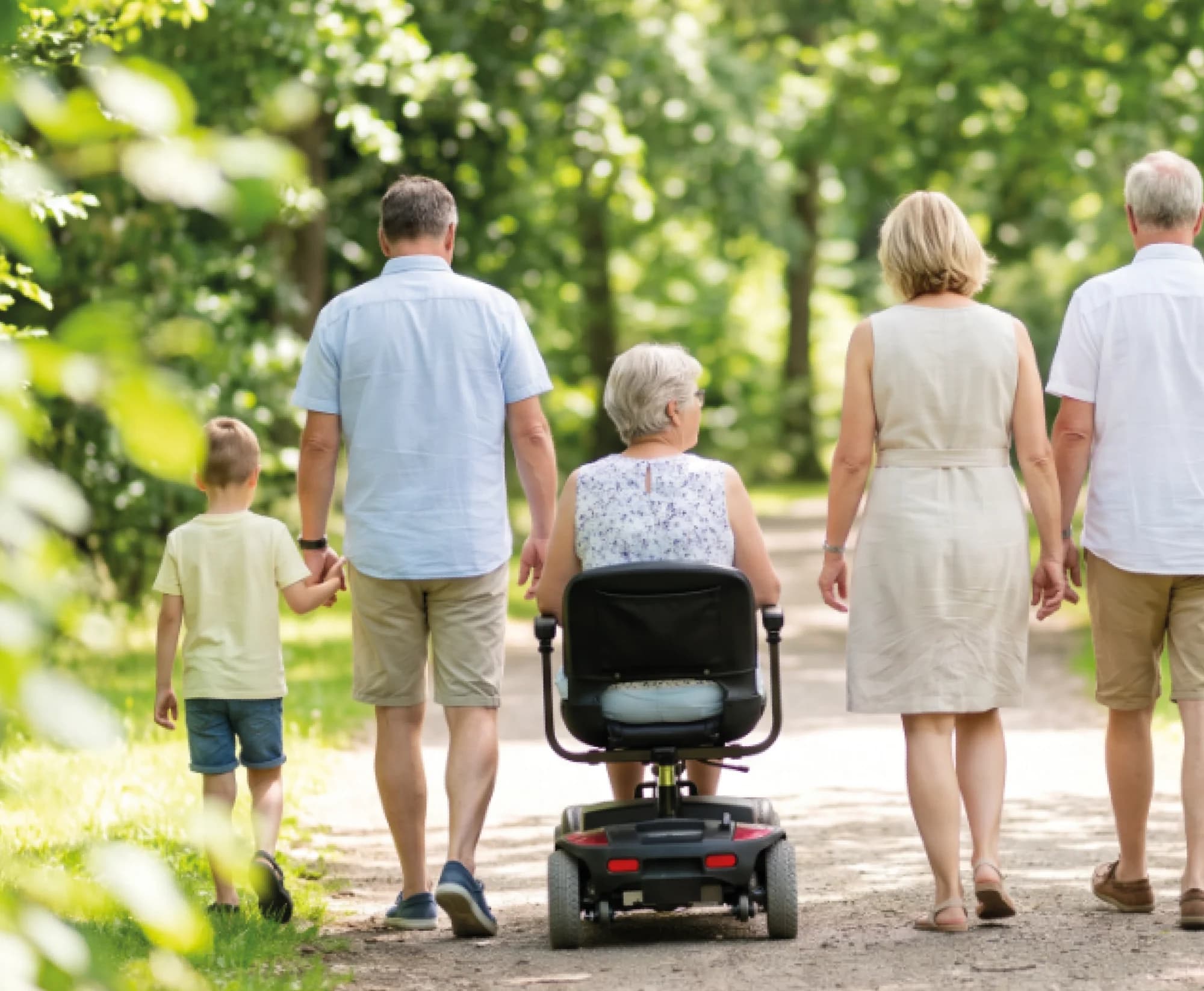 A family walking together along a tree-lined path, one of them on a mobility scooter